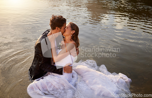 Image of Wedding, kiss and couple in the water of a lake to celebrate their sunset marriage outdoor in nature. Happy, love and young wet man and woman being intimate for romantic playful outdoor celebration.