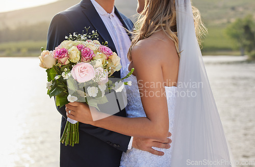 Image of Flower bouquet, wedding and hug with couple in nature for commitment, romantic ceremony or union event. Outdoor lake, love and countryside marriage of man and woman hugging in solidarity and support