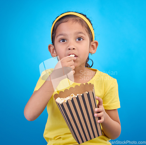 Image of Popcorn, eating and focus with girl in studio for food, cinema and relax. Television, movie and film with child and snack for streaming service, subscription and tv isolated on blue background