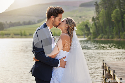 Image of Love, wedding and a married couple kissing by a lake outdoor in celebration of their marriage for romance. Water, summer or kiss with a bride and groom bonding together in tradition after ceremony