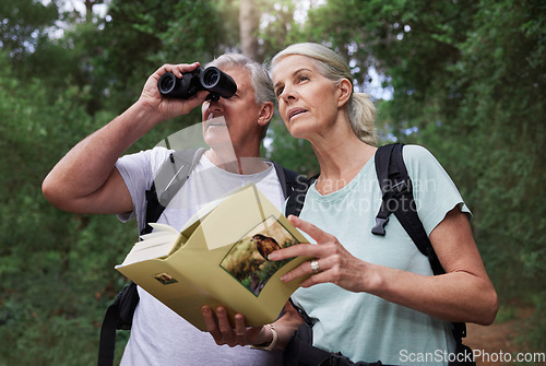 Image of Book, bird watching and binoculars with old couple in nature for bonding, discovery and travel adventure. Search, hiking and view with senior man and woman in forest for explore, retirement and hobby