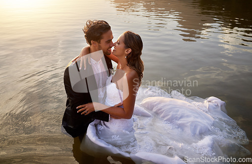 Image of Wedding, water and wet bride with groom hug, kiss and standing in lake together with passion, smile and romance. Love, marriage and happy couple celebrate romantic, loving relationship in nature.