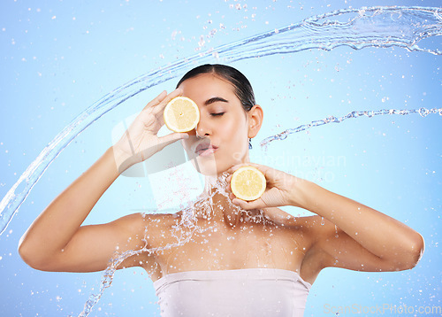 Image of Beauty, water splash and lemon with woman in studio for natural cosmetics, nutrition and detox. Glow, fruits and hydration with female and pouting on blue background for vitamin c, face and skincare