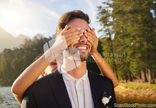 Image of Love, wedding or surprise with a bride and groom by a lake, in celebration of a ceremony of tradition. Romance, marriage and hands over face with a married couple playing or joking together outdoor