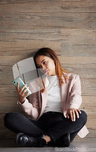 Image of Young business woman, floor and texting with bored face on social media, app or phone in modern office. Professional female, smartphone and tired with search for email, chat or communication on break