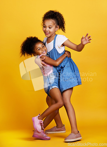 Image of Children, hug and happy sisters in studio dancing with love, care and support of family on yellow background. Cute young girl kids play together for happiness, fun and positive attitude or fashion