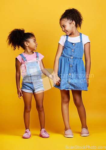 Image of Children, holding hands and happy sisters in studio with love, care and support of family on yellow background. Cute young girl kids or friends together for happiness, positive attitude or trust