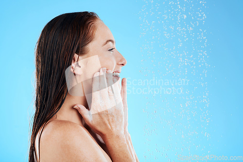 Image of Shower, water and happy woman with soap on face in studio, blue background and skincare cleaning. Female model washing facial with foam, wet drops and beauty of self care, glow and smile on backdrop