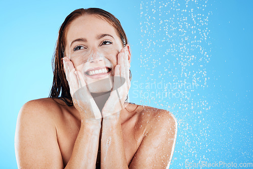 Image of Shower, water and face of happy woman with soap in studio, blue background and skincare cleaning. Female model washing facial with foam, wet drops and beauty of self care, glow and smile on backdrop
