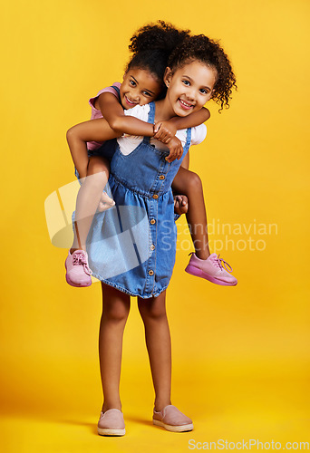 Image of Children, portrait and happy sisters for piggyback fun in studio with love of family on yellow background. Cute young girl kids or friends smile together for happiness, play and support or care