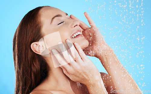 Image of Shower, water and smile of woman in studio, blue background and cleaning for hygiene. Happy female model washing with wet drops for beauty, skincare and grooming for self care, wellness and routine