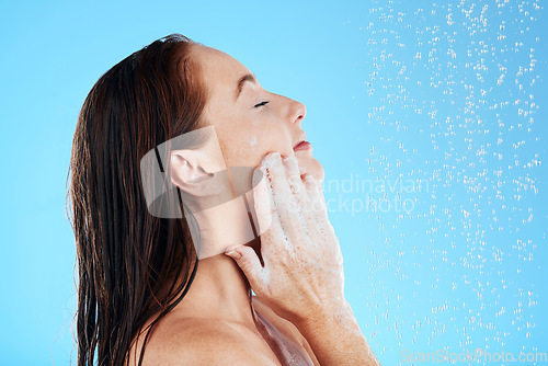 Image of Shower, water and woman soap on face in studio, blue background and hygiene cleaning. Relax female model washing facial with wet drops, foam and beauty of skincare cosmetics, self care and backdrop