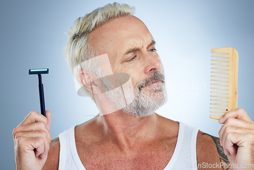 Image of Mature man, shaver and comb thinking for grooming, skincare or hair removal against studio background. thoughtful senior male holding razor blade and brush for haircare, cosmetics or facial treatment