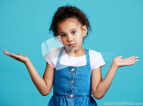 Image of Portrait, children and shrug with a girl on a blue background in studio feeling confused or lost. Kids, question and doubt with a young female child shrugging her shoulders to gesture whatever