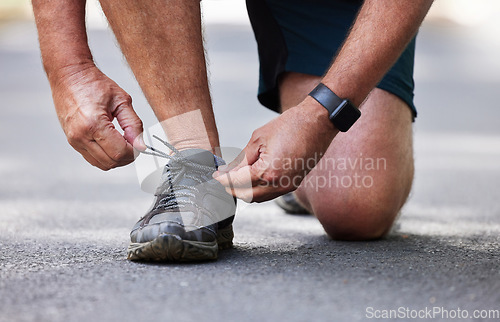 Image of Hands, shoes and running with a senior man tying his laces outdoor on a road during a cardio workout. Fitness, exercise or footwear with a male runner getting ready for endurance training on a street