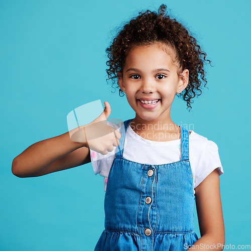 Image of Happy, portrait and girl child with thumbs up in a studio with success, happiness and achievement. Smile, positive and face of a kid with a satisfaction or approval hand gesture by a blue background.