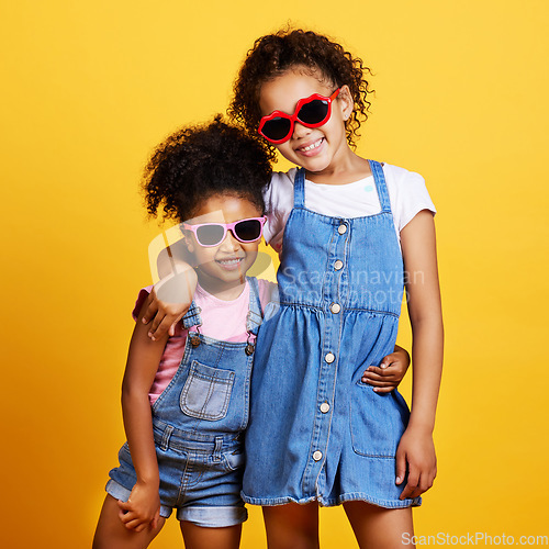 Image of Children, sunglasses and happy sisters in studio hug for love, care and support of family on yellow background. Cute young girl kids portrait together for happiness, carefree and fashion with a smile