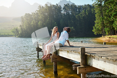 Image of Young couple, lake and jetty with laughing, happiness and bonding with love in nature for holiday. Man, woman and comic joke on bridge by water to relax with conversation, care and vacation in summer