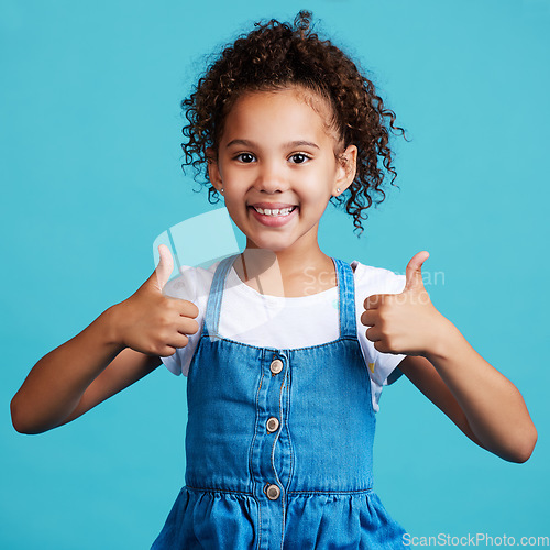 Image of Smile thumbs up and portrait of a kid in a studio with success, happiness and achievement. Happy, positive and face of a girl child with a satisfaction or approval hand gesture by a blue background.