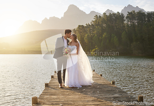 Image of Kiss, romantic and a married couple on a pier over a lake in nature with a forest in the background after a ceremony. Wedding, love or water with a bride and groom in celebration of marriage outdoor