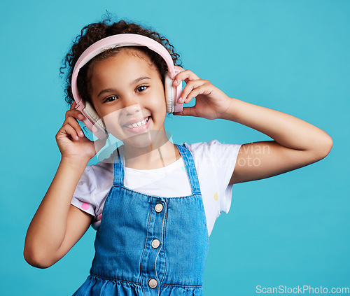 Image of Music, portrait and girl child with headphones in studio for streaming, subscription and audio on blue background. Face, autism and autistic kid happy with noise canceling headphone while isolated