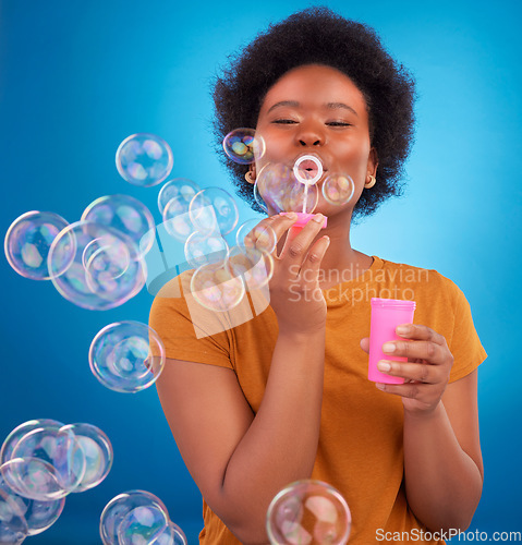 Image of Fun, bubbles and black woman with joy, positive attitude and happiness against a blue studio background. African American female, lady and soap bubble for joy, playing and cheerful with excitement