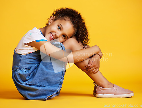 Image of Portrait, happy and girl child on studio floor for children fashion, playful and sweet against yellow background. Face, little and smile by kid with self love, pose and relax while sitting isolated