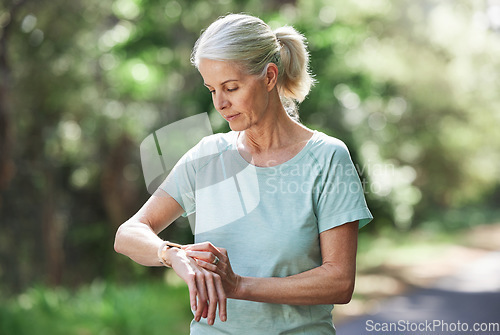 Image of Senior woman, watch and outdoor for exercise time on run, workout and training on road for fitness. Elderly female person check cardio progress for health and wellness while running in nature