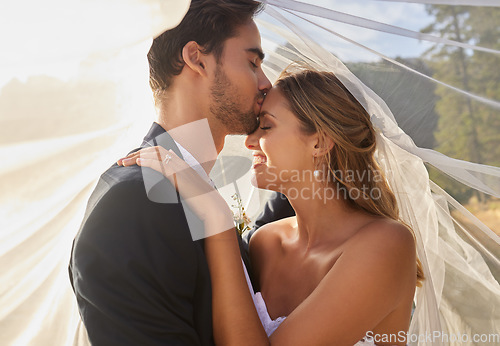 Image of Couple, wedding and forehead kiss with vail for love, compassion or affection together in nature. Marred man kissing woman on head and hugging in marriage, relationship or loving embrace outdoors