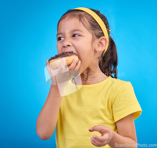 Image of Donut, eating and sweet with girl in studio for junk food, sugar and happiness. Snack, cake and cute with face of child and dessert for candy diet and chocolate isolated on blue background