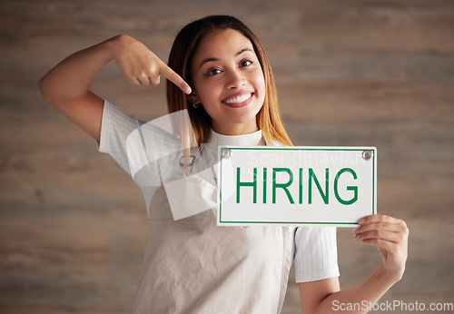 Image of Happy woman, portrait and pointing to hiring sign for small business recruitment, career or job opportunity against studio background. Female entrepreneur with apron holding billboard poster for hire