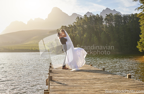 Image of Kiss, dance and a married couple on a pier over a lake in nature with a forest in the background after a ceremony. Wedding, love or water with a bride and groom in celebration of marriage outdoor