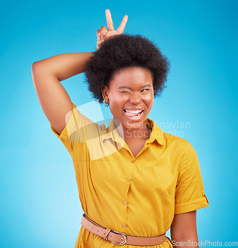 Image of Silly, peace sign and woman in a studio feeling fun, playful and funny with a blue background. V hand gesture, bunny ears and tongue out for comedy with a young female model smile with happiness