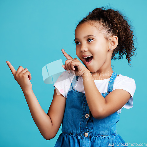 Image of Wow, pointing and a girl on a blue background in studio for marketing with product placement space. Kids, surprise and hand gesture with an adorable little female child showing mockup for advertising