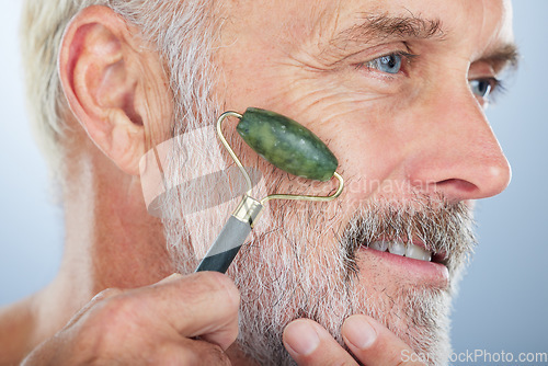 Image of Elderly man, jade roller and face for skincare with smile, self care and wellness in studio by white background. Elderly model, facial massage and beauty with stone product, cosmetic and dermatology