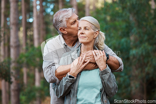 Image of Hiking, kiss and senior couple with love in a forest, relax and hug while standing in nature park together. Caring, embrace and sweet, elderly man with woman on retirement vacation in the woods