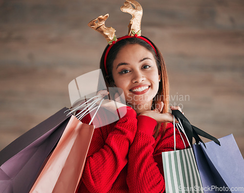 Image of Shopping bags, portrait and woman with a christmas headband for a festive or holiday celebration. Happy, smile and face of a female model with gifts or presents with xmas reindeer ears for an event.