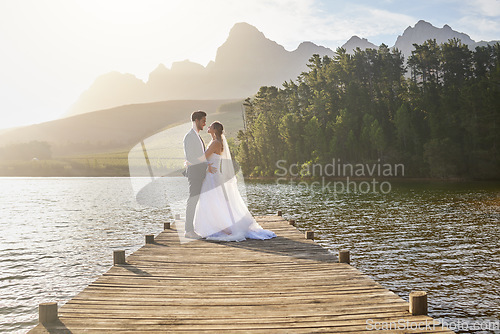 Image of Married, bride and groom on a pier over a lake in nature with a forest in the background after their ceremony. Wedding, love and water with a young couple in celebration of their marriage outdoor