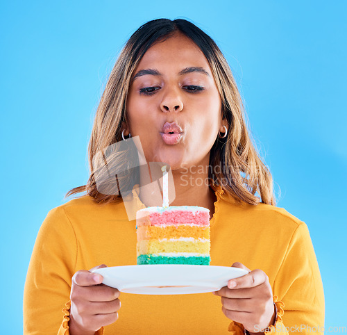 Image of Birthday cake, candle blowing and woman in a studio with celebration and dessert. Party food, isolated and blue background of a young female with sweet and rainbow treat with surprise and plate