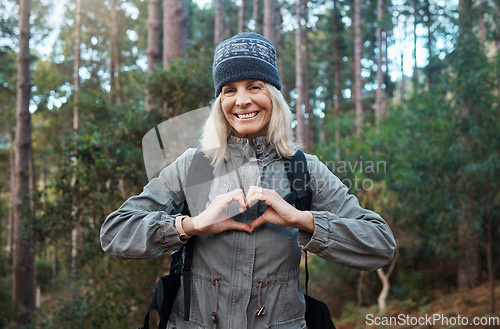 Image of Portrait, heart and happy woman in forest hiking, fitness and health support, self care hands and cardiovascular workout. Nature, travel or trekking of mature person in woods with love sign or emoji