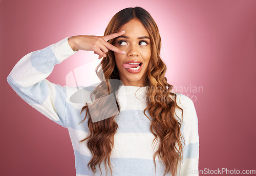 Image of Comic face, peace sign and tongue of a woman in studio on a gradient pink background feeling silly. Young female fashion model looking playful and having fun with hand on eyes for cute or goofy emoji