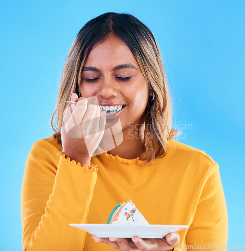 Image of Birthday, blue background and a woman eating cake in studio while having fun at a party for celebration. Dessert, food and fork with an attractive young female enjoying a rainbow pastry snack