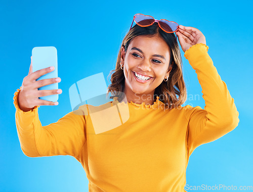 Image of Woman, face and smile in studio for selfie, social media or vlog in happiness and style against a blue background. Happy isolated female influencer smiling for picture photo, memory or online post