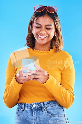 Image of Woman, phone and smile for social media, communication or chatting isolated against a blue studio background. Happy female smiling with teeth texting on mobile smartphone in happiness for online chat