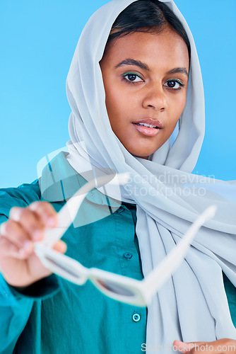 Image of Fashion glasses, face portrait and muslim woman with hijab, trendy designer brand or casual outfit style. Gen z aesthetic, Islamic person giving sunglasses and Arab female on blue background studio