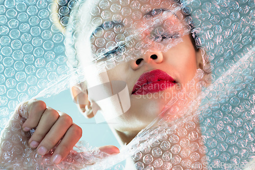 Image of Beauty, bubble wrap and makeup with breakthrough with woman for package, creative and cosmetics. Plastic, confidence and face with female model and red lipstick for facial, art and glow in studio