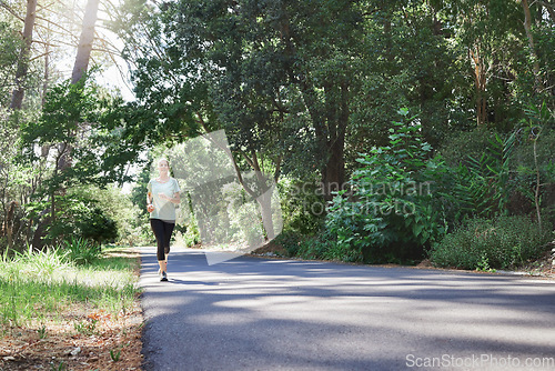 Image of Fitness, workout and a running senior woman on a road through a forest or park for cardio and endurance. Exercise, mockup and health with a mature female runner or athlete training outdoor in nature