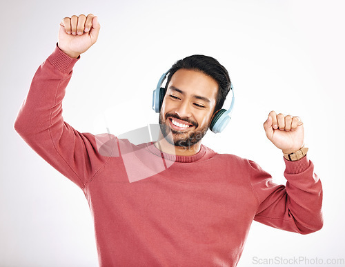 Image of Headphones, happy and man dancing in a studio to music, playlist or album for entertainment. Happiness, dance and Indian male model moving to the radio or streaming a song by a white background.