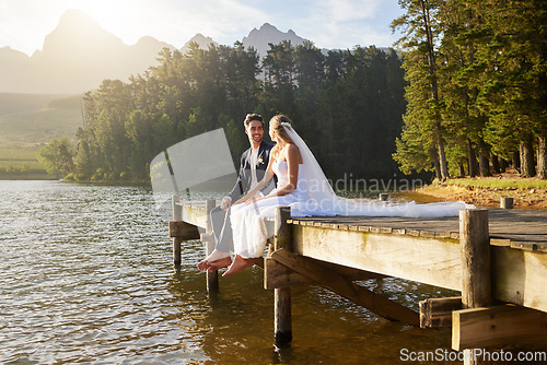 Image of Forest, lake and a married couple on a pier in celebration together after a wedding ceremony of tradition. Marriage, love or romance with a bride and groom sitting outdoor while bonding in nature