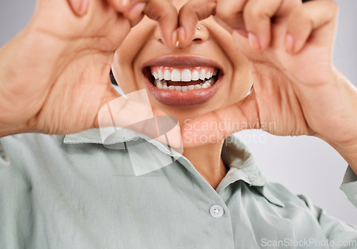 Image of Love, smile and hands of a black woman with a heart isolated on a studio background. Happy, mouth and closeup of an African girl showing a shape for dental care, oral hygiene and teeth whitening